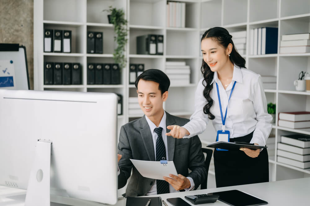 A male and female coworker looking at a big computer monitor and smiling.